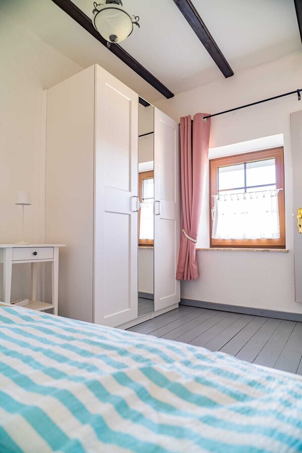 Un dormitorio con cama, armario, mesita de noche, ventana con cortinas e iluminación en el techo.
