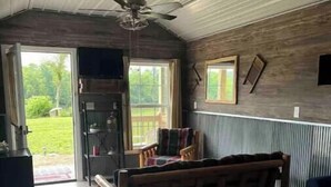 Un dormitorio con cama, cabecera de madera, ventilador de techo, ventana y puerta que da a un balcón.