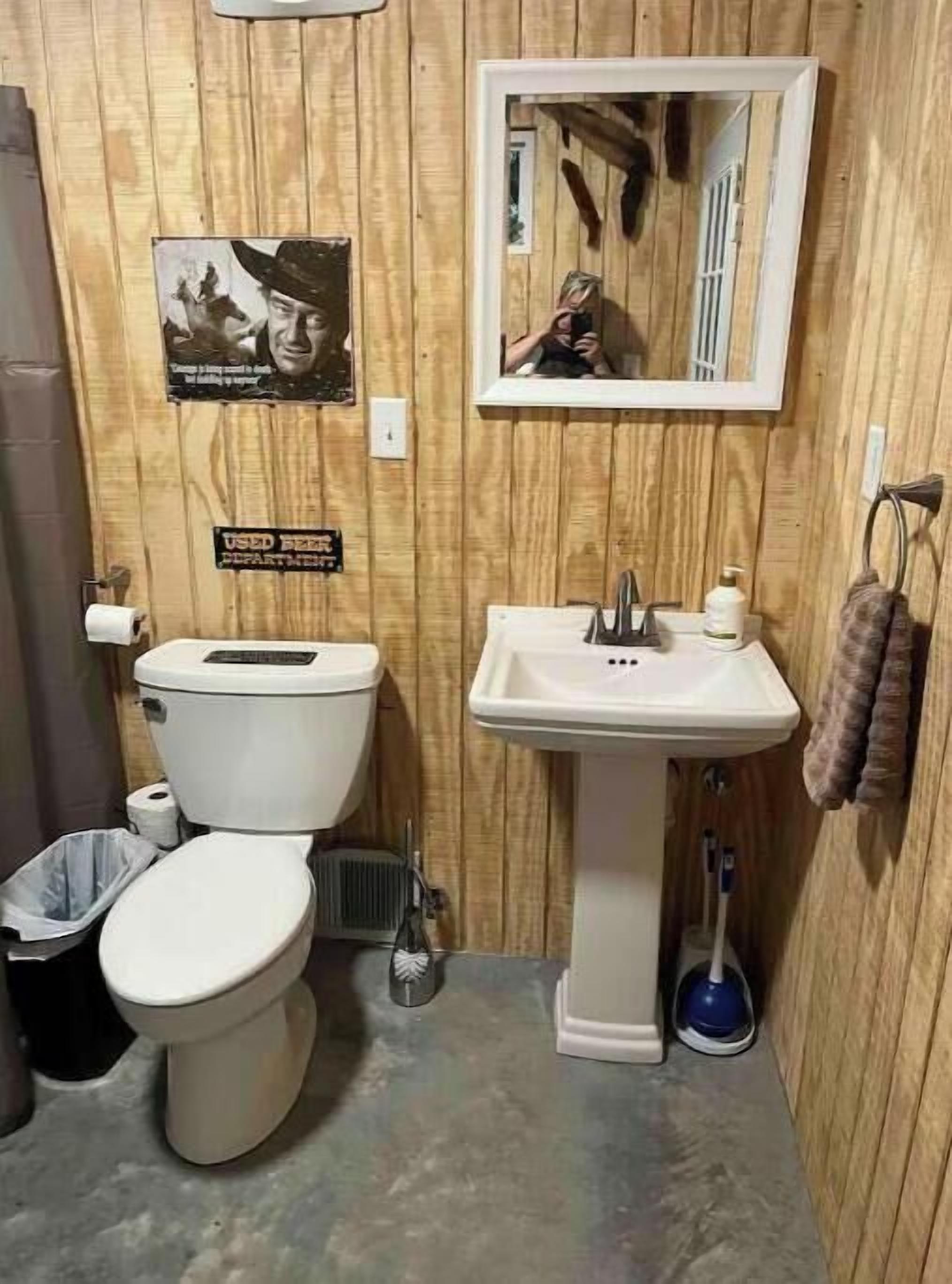 Une petite salle de bain aux murs lambrissés, équipée de toilettes, d’un lavabo et d’un miroir.