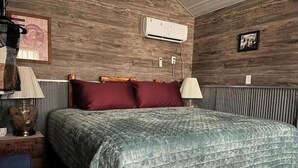 Un dormitorio con pared de madera, una cama con cubrecama acolchado, una lámpara y un marco de cuadro.