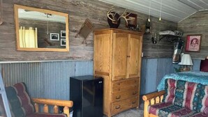 Una habitación rústica con un armario de madera, un refrigerador negro pequeño, un sofá colorido y un espejo en la pared.