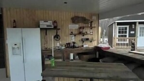 Een compacte keuken met een koelkast, houten kastjes en een eethoek met een tafel en stoelen.