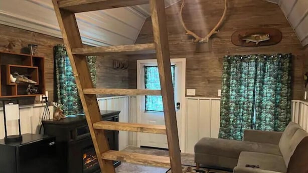 Een rustiek interieur met een houten ladder, een open haard, een bank en een decoratie van een hertenkop.