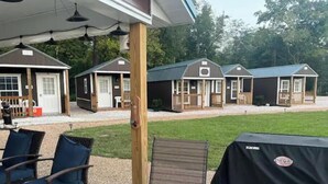 Een overdekt terras met buitenmeubilair, een barbecue en uitzicht op een woonwijk.