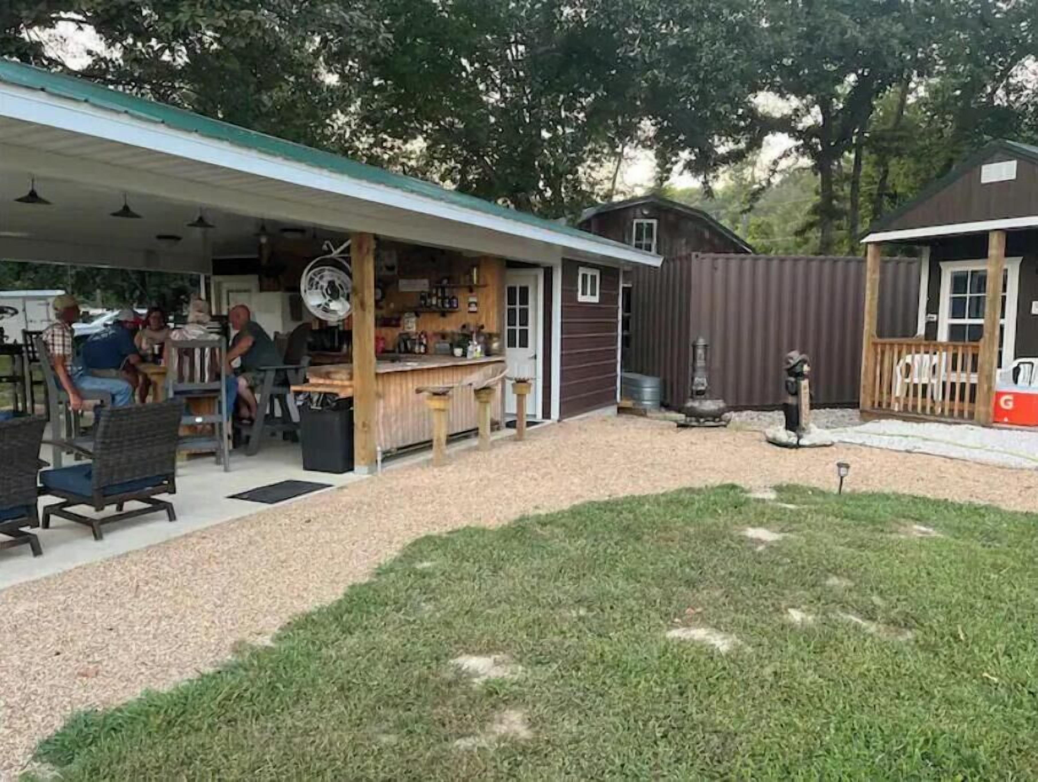 Un espace extérieur abrité, doté d’un bar et de sièges, entouré d’une cour clôturée et d’une maison.