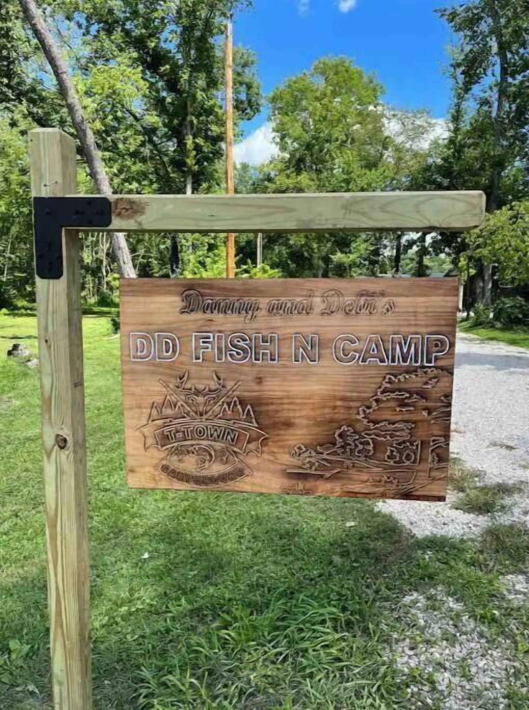 A wooden sign for DD Fish N Camp with a mountain and fishing boat illustration.
