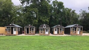 Una fila di piccole cabine a un piano con veranda, immerse in un'area erbosa con alberi sullo sfondo.