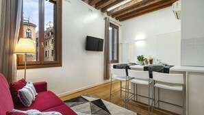 Una sala de estar moderna con un sofá rojo, un tapete estampado y una zona de cocina con taburetes blancos.
