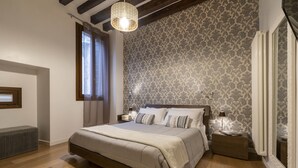 Un dormitorio con una cama grande, suelo de madera, papel tapiz estampado y una lámpara colgante.