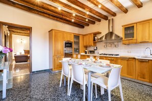 A modern kitchen with wooden cabinets, granite countertops, and a dining area with a glass table and white chairs. - Al Campanile View Terrace by Wonderful Italy (Venice)