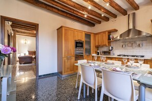 A modern kitchen with wooden cabinets, stainless steel appliances, and a dining area with a glass table and white chairs. - Al Campanile View Terrace by Wonderful Italy (Venice)