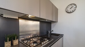 A modern kitchen with a stainless steel gas stove, a clock on the wall, and herb containers on the counter. - Arsenale Canal View 1 by Wonderful Italy (Venice)