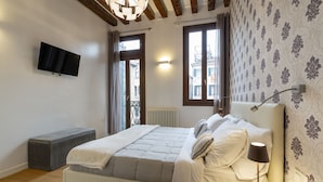 Een moderne slaapkamer met een bed, nachtkastje, lamp en een aan de muur bevestigde televisie.