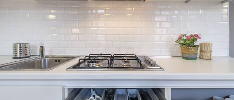 A modern kitchen with white tiles, stainless steel appliances, and a built-in drawer for utensils.