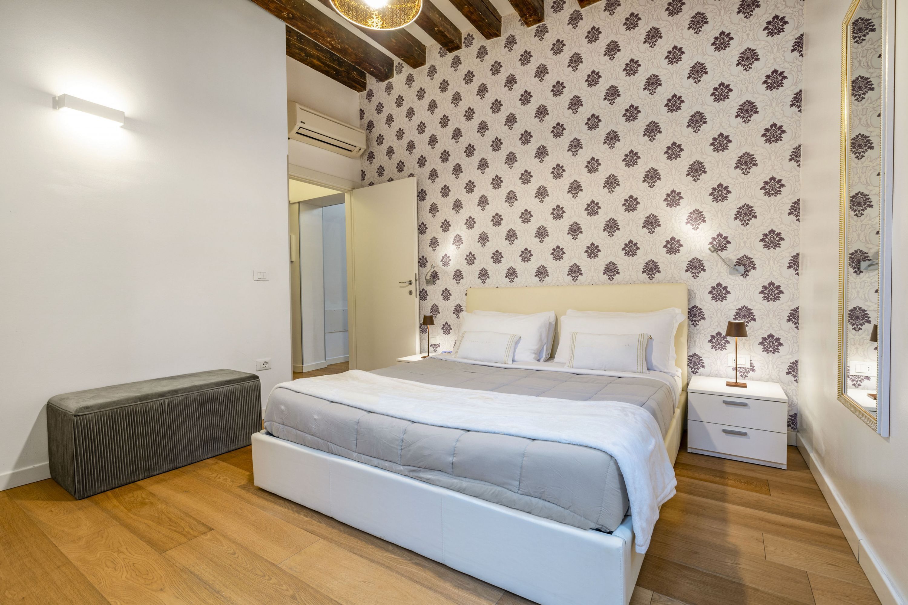 Un dormitorio con una cama grande, una mesita de noche, un radiador y un espejo en la pared.