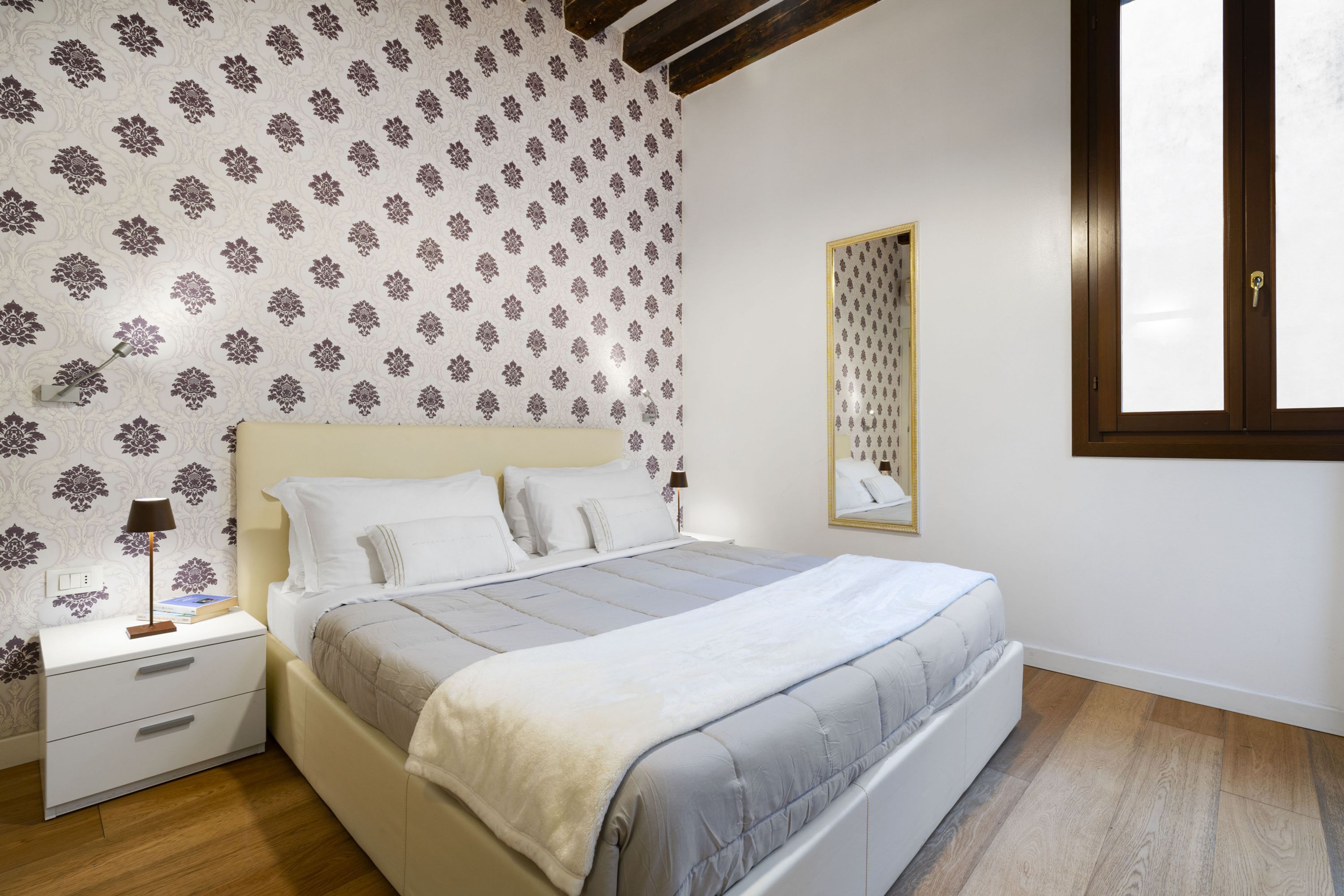 A bedroom with a bed, nightstands, a mirror, and a window.