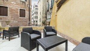 An outdoor seating area with wicker furniture and a tiled floor, surrounded by buildings with varying architectural styles. - Gondola Luxury Apartment by Wonderful Italy (Venice)