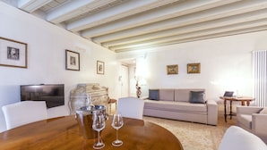 A modern living room with a wooden dining table, white sofas, and a flat-screen TV. - Gondola Luxury Apartment by Wonderful Italy (Venice)