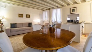 A modern living room with a round wooden table, white sofas, and a kitchen area in the background. - Gondola Luxury Apartment by Wonderful Italy (Venice)
