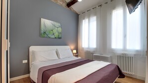 Un dormitorio con cama, un cuadro en la pared, una ventana con cortinas y un radiador.