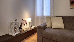 Una sala de estar con un sofá marrón, dos almohadas, una lámpara de mesa blanca y un farol blanco, además de una orquídea en maceta.