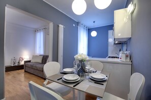 Ein moderner Essbereich mit Tisch für vier Personen, einer Couch im Hintergrund und einer Küchenzeile inklusive Mikrowelle und Toaster.