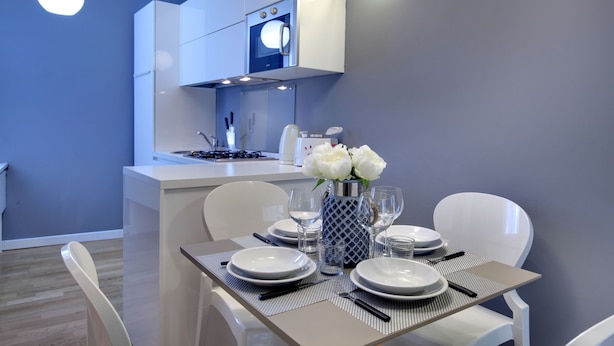 Una cocina moderna con armarios blancos, horno empotrado y un comedor con mesa preparada para cuatro.