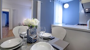 Comedor con una mesa dispuesta para cuatro, un florero con flores blancas, y una cocina visible al fondo.
