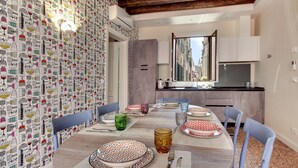 A dining area with a round table set for six, surrounded by chairs. A kitchen with a large window is visible in the background. - Rugabella Rialto by Wonderful Italy (Venice)