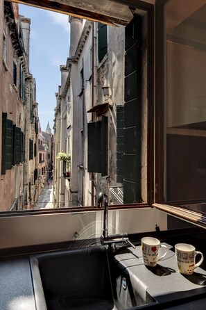 Blick aus einem Fenster auf eine enge Gasse, auf der Ablage ein Waschbecken und zwei Tassen.