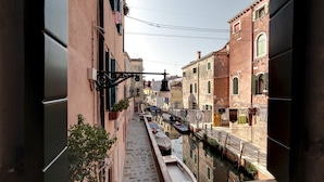 A narrow canal with buildings on either side, a boat docked on the right, and a staircase leading down to the water. - Laguna Luxury 1 by Wonderful Italy (Venice)