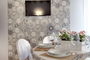 Ein Essbereich mit einem Tisch für vier Personen, gedeckt mit Tellern, Besteck und Gläsern. Ein Flachbildfernseher ist über dem Tisch an der Wand befestigt.