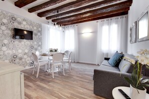 Un salon moderne comprenant un coin repas, un parquet, un téléviseur à écran plat fixé au mur et un canapé gris agrémenté d’une plante.