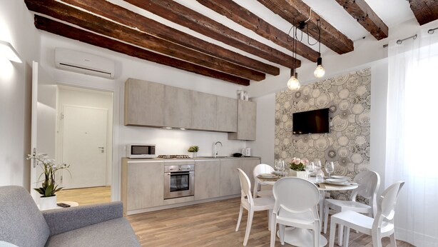 A modern kitchen with wooden beams, a dining area with white chairs, and a TV mounted on the wall. - Laguna Luxury 1 by Wonderful Italy (Venice)