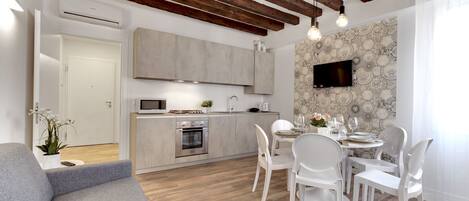 Una cocina moderna con vigas de madera, un comedor con sillas blancas y un televisor montado en la pared.