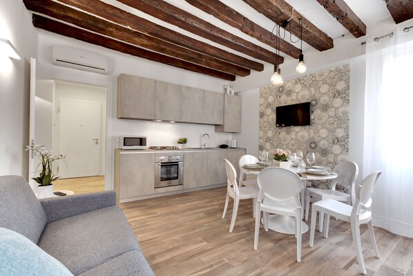 Una cocina moderna con vigas de madera, un comedor con sillas blancas y un televisor montado en la pared.