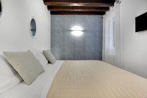 Un dormitorio con cama, almohadas, una lámpara de pared y un papel tapiz estampado.