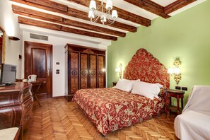 Une pièce avec un plafond en bois, un lit recouvert d’une couvre-lit aux motifs rouges et dorés, une commode en bois, un bureau avec une chaise et un mur vert agrémenté d’une tête de lit décorative.