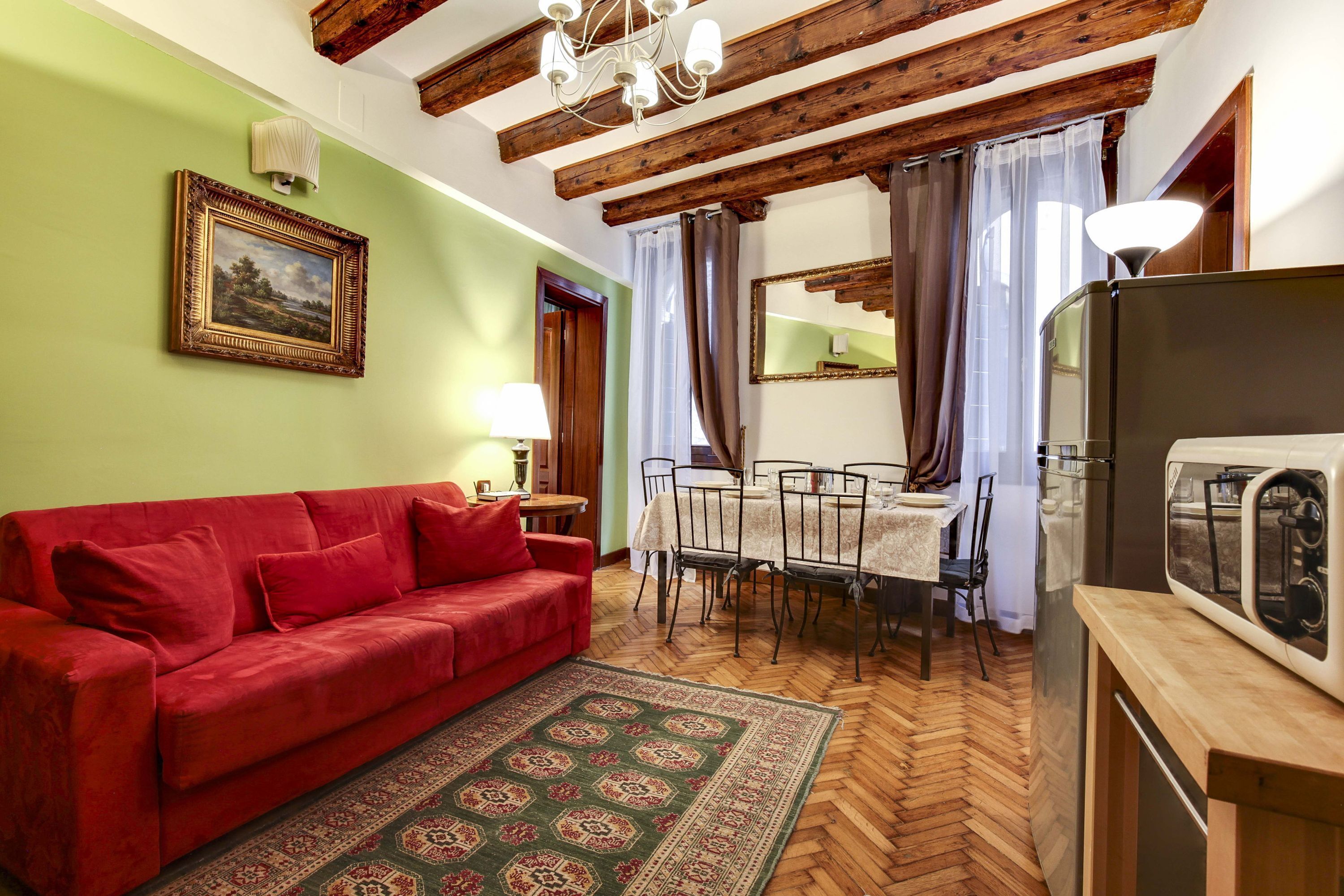 A cozy living room with a red sofa, wooden floor, and a dining area with a table and chairs.