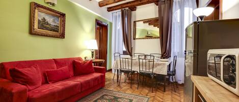 A cozy living room with a red sofa, wooden floor, and a dining area with a table and chairs.
