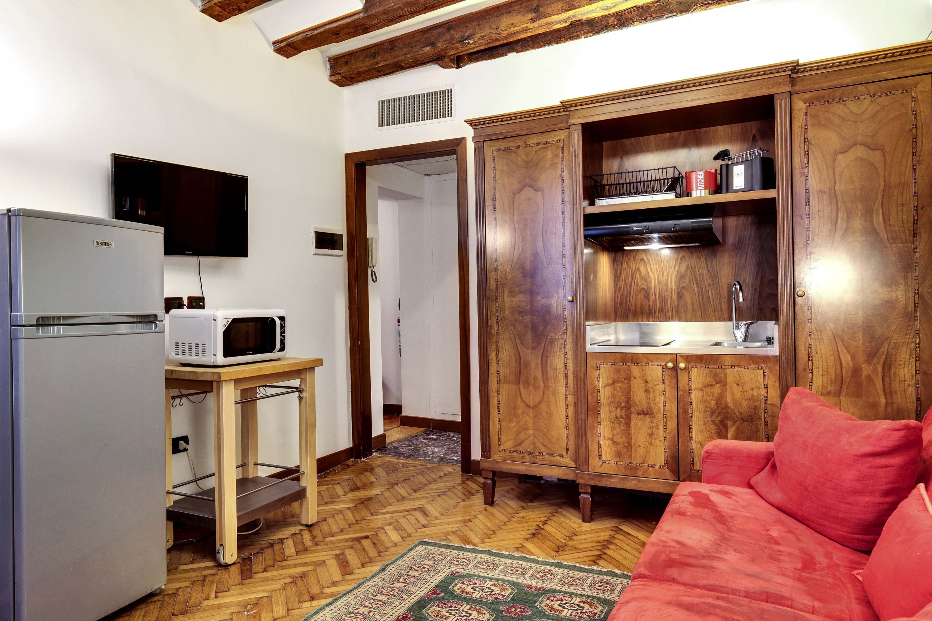 A compact living space with a kitchenette, a microwave, a refrigerator, a television, and a red sofa.