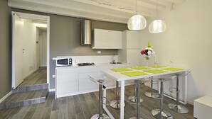 Una cocina moderna con armarios blancos, campana de acero inoxidable y un área de comedor con mesa blanca y taburetes de bar.