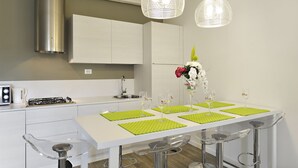 Una cocina moderna con armarios blancos, una campana de acero inoxidable y un comedor con una mesa blanca y manteles individuales verdes.