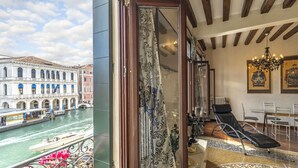 A room with a view of a canal, a balcony with flowers, and a lounge area with a chair and table. - Rialto Grand Canal - Locz (Venice)