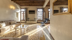 A living room with a sofa, coffee table, and a chair. There is a television mounted on the wall and a large mirror on the wall. - Rialto Grand Canal - Locz (Venice)