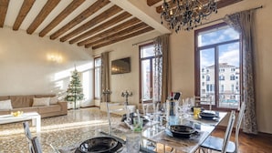 A dining area with a wooden ceiling, a chandelier, and a view of buildings through large windows. - Rialto Grand Canal - Locz (Venice)