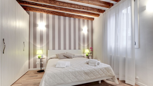Une chambre avec un plafond en bois, un lit avec une literie blanche, deux lampes de chevet et un mur à rayures.