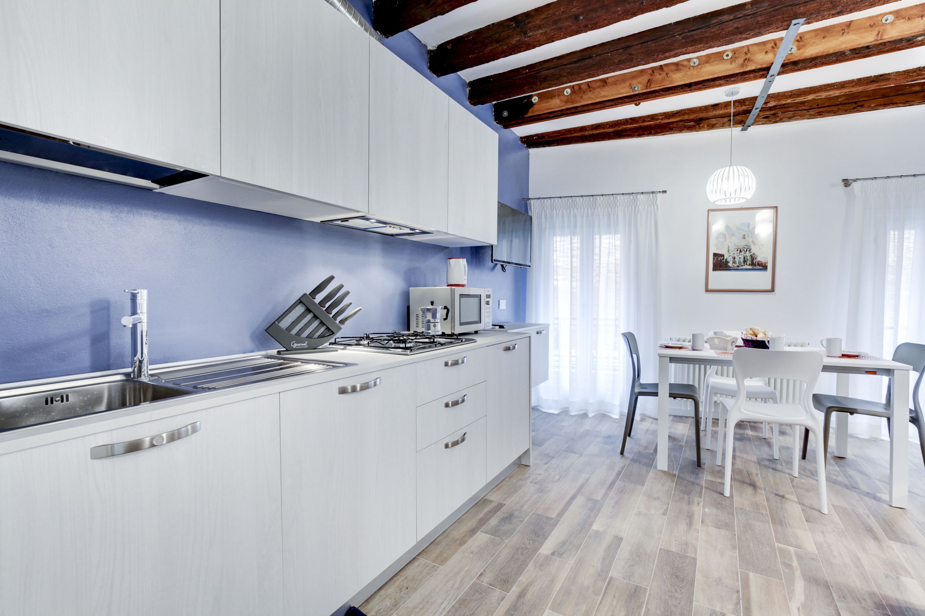Una cocina moderna con armarios blancos, una estufa a gas y un microondas. Hay una zona de comedor con una mesa y sillas.