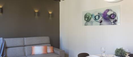 A modern living room with a grey sofa, a dining table set with plates, glasses, and cutlery, and a painting on the wall.