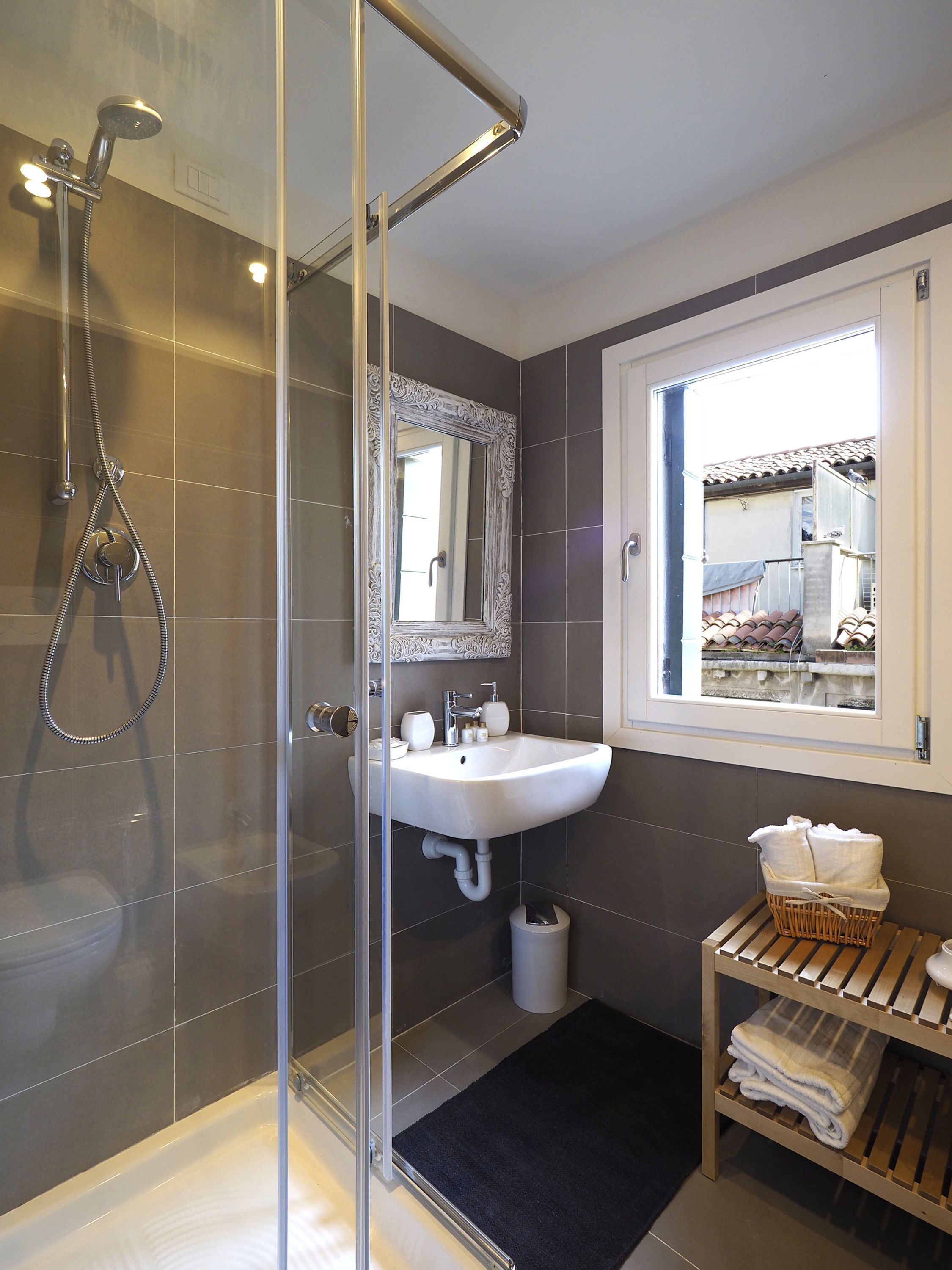 A modern bathroom with a glass-enclosed shower, a white sink, and a window with a view of the outside.